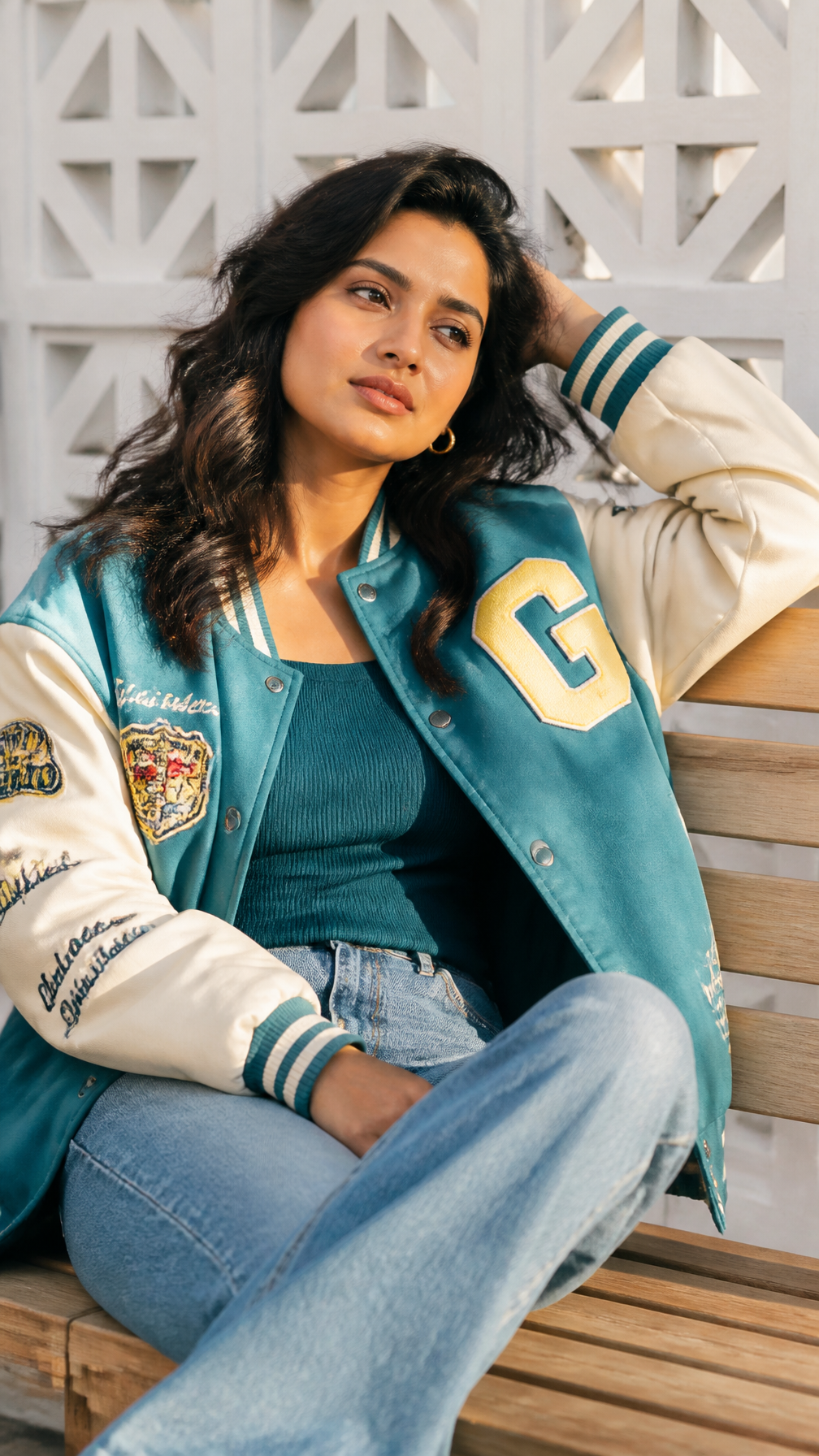 Young Woman in Teal Varsity Jacket on Wooden Bench
