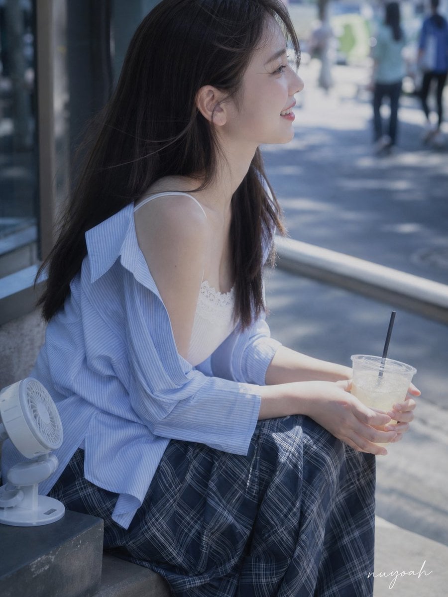 成年年轻女性，清透桃粉甜美妆，深棕长直发与自然风吹碎发，白色蕾丝吊带搭配宽松浅蓝条纹衬衫、深蓝格纹下装；盛夏城市街... - alternate