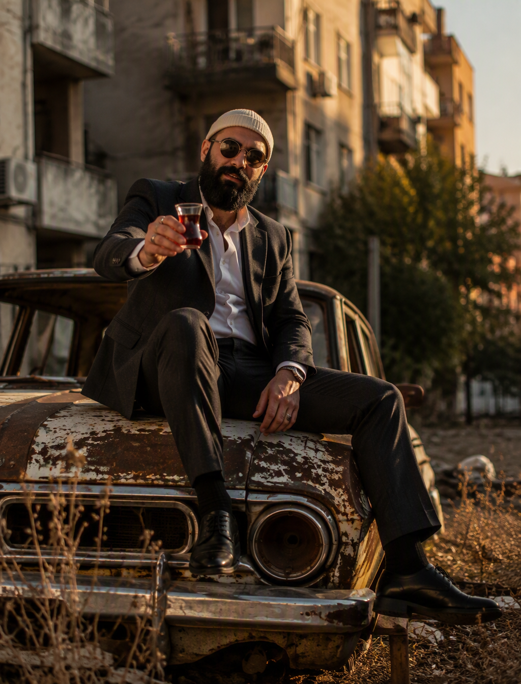 A bearded man in a cream ribbed beanie, round sunglasses,...