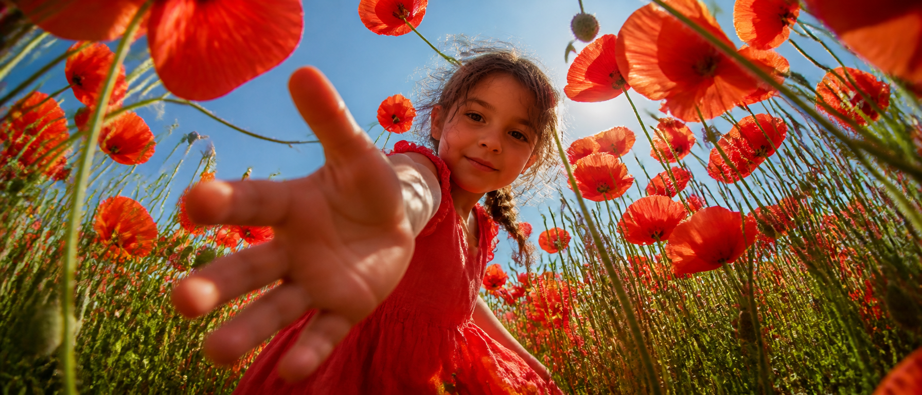 A young girl in a coral-red dress leans over the camera i...