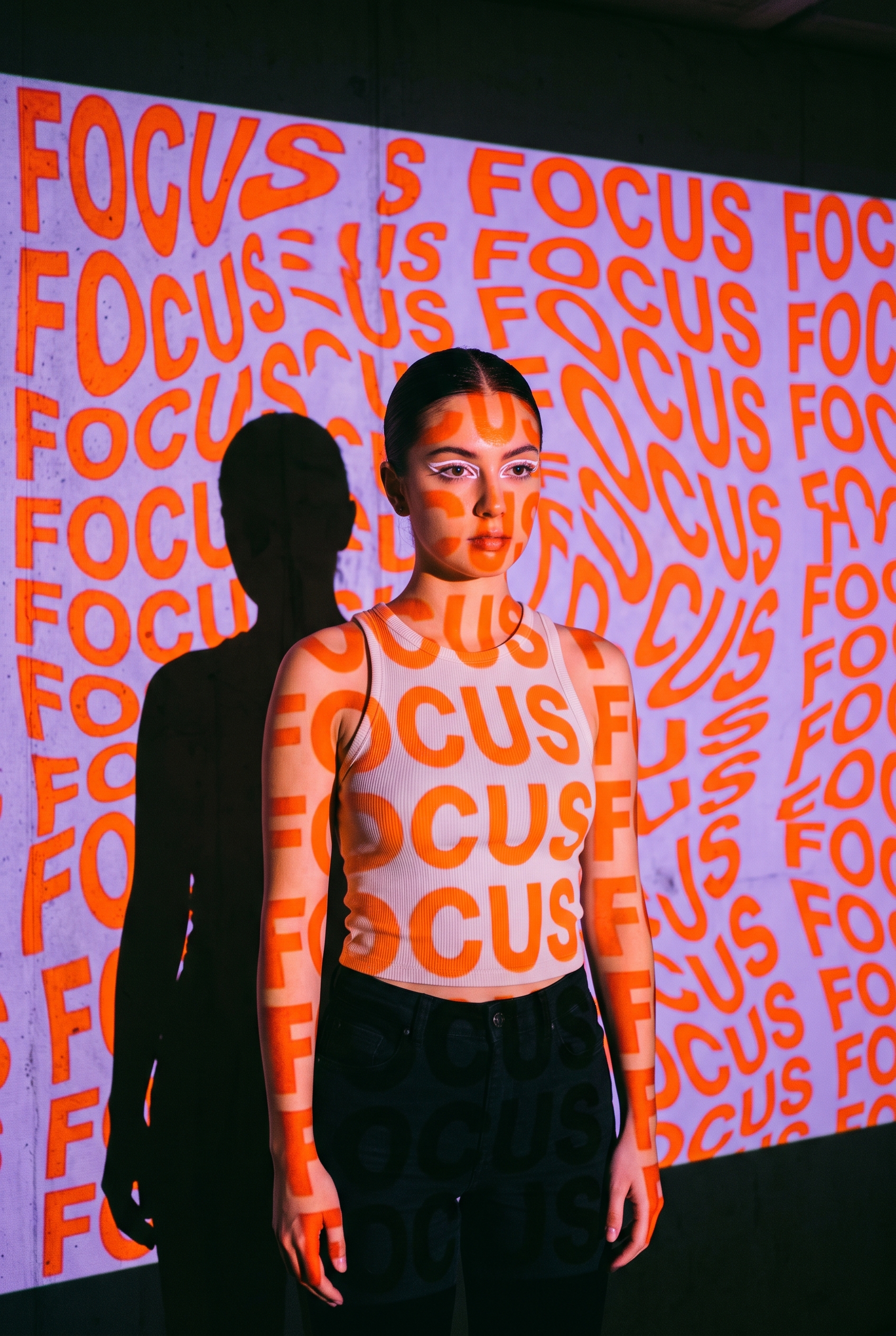 A young woman stands in front of a wall with a projection...